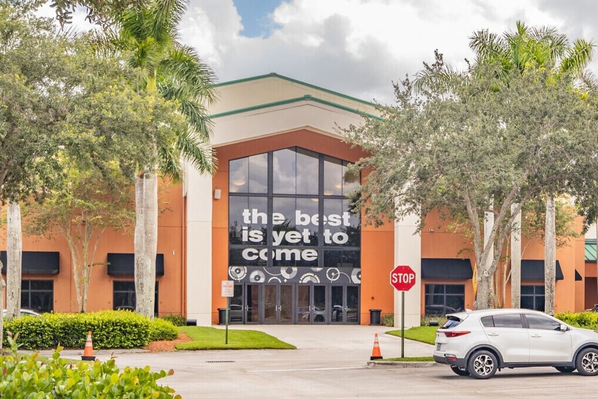 Front of a modern orange and beige building with a large glass entry displaying the slogan 'the best is yet to come'.